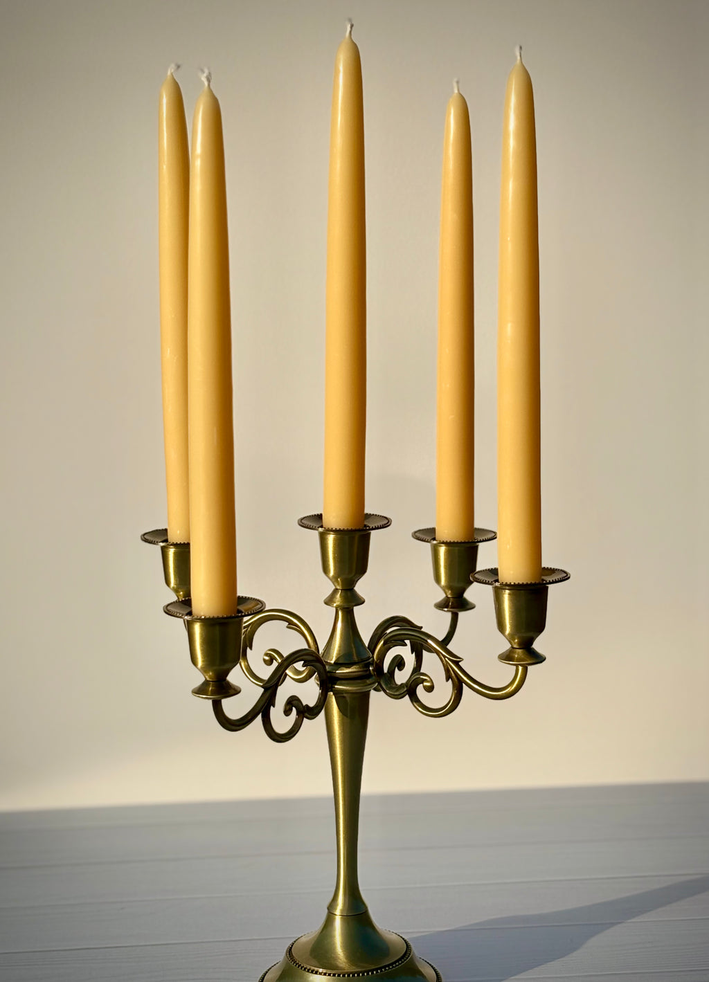 Gold candelabra with five tall, thin candles on a neutral background