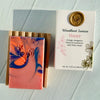 Marbled soap bar with a wooden holder and 'Woodland Sunrise' packaging on a light background