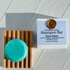 Shampoo bar with packaging labeled 'Woodland Sunrise Notre Dame' on a wooden stand.