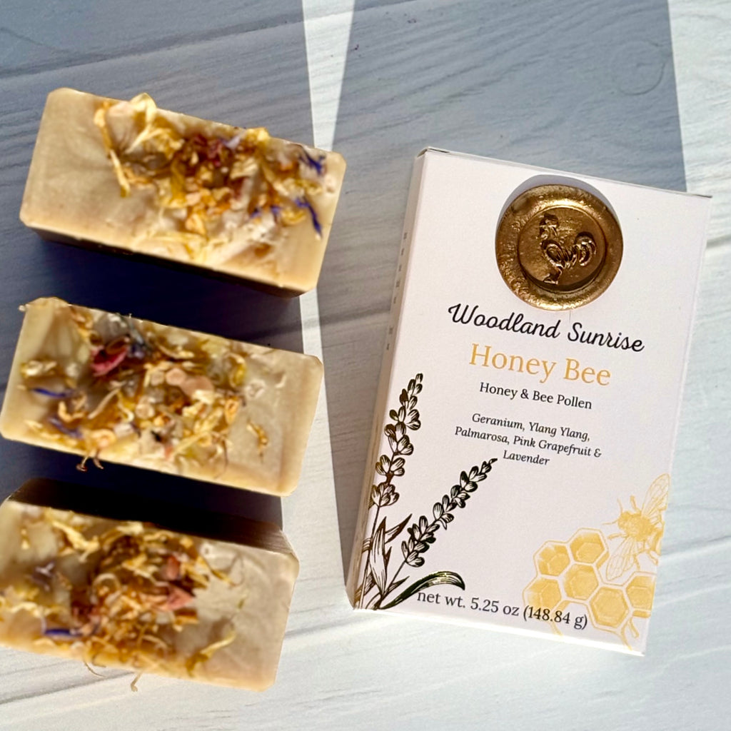 Three bars of 'Woodland Sunrise Honey Bee' soap with packaging on a light wooden surface.