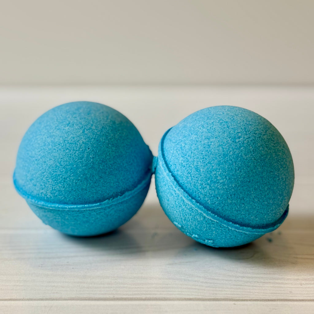 Two blue bath bombs on a light wooden surface
