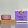 Purple shampoo bar with packaging labeled 'Woodland Sunrise Shampoo Bar Lavender Moonlight' on a gray background