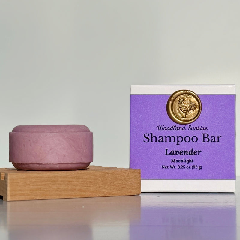 Purple shampoo bar with packaging labeled 'Woodland Sunrise Shampoo Bar Lavender Moonlight' on a gray background