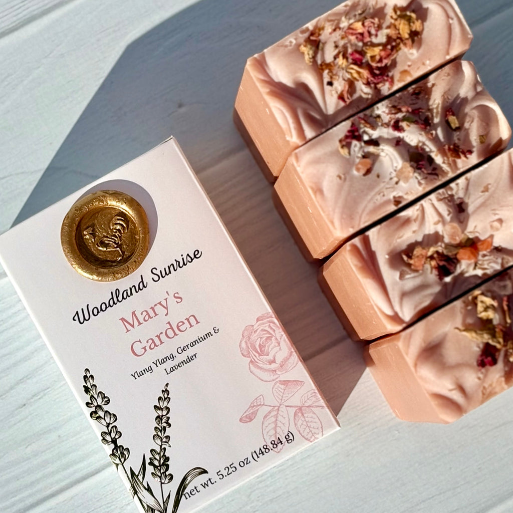Bar soaps with floral elements next to their packaging labeled 'Woodland Sunrise Mary's Garden'.