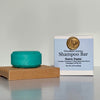 Teal shampoo bar on a wooden block with a label in the background