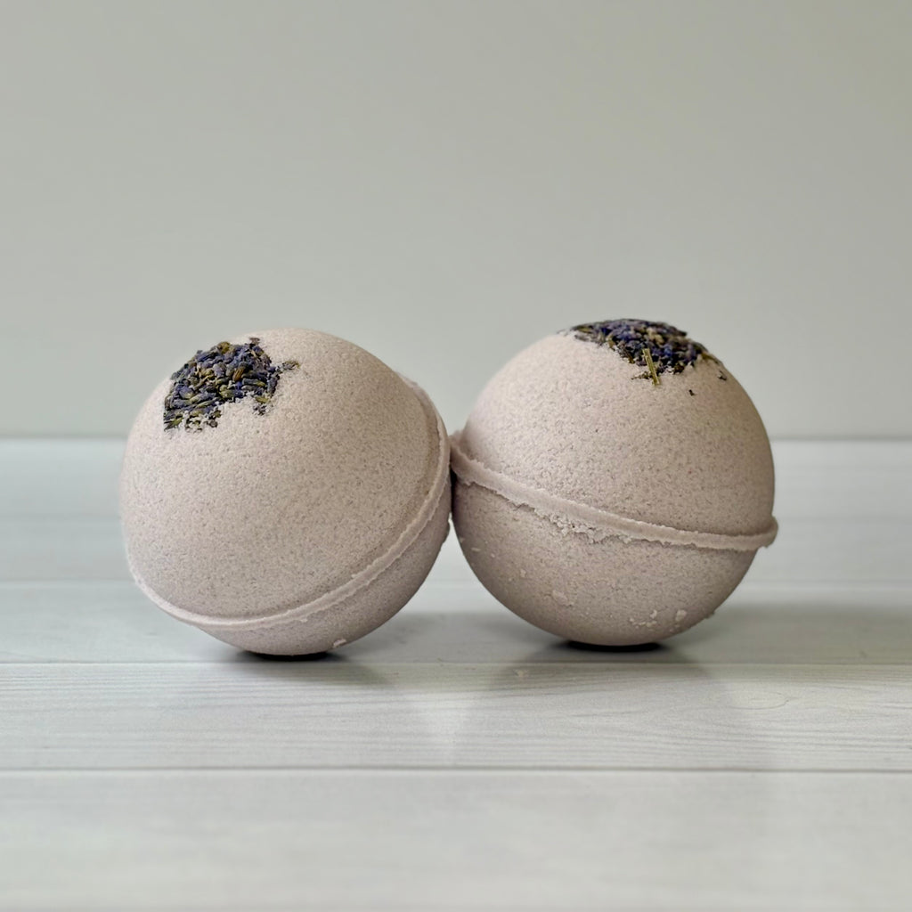 Two bath bombs with lavender buds on a light wooden surface