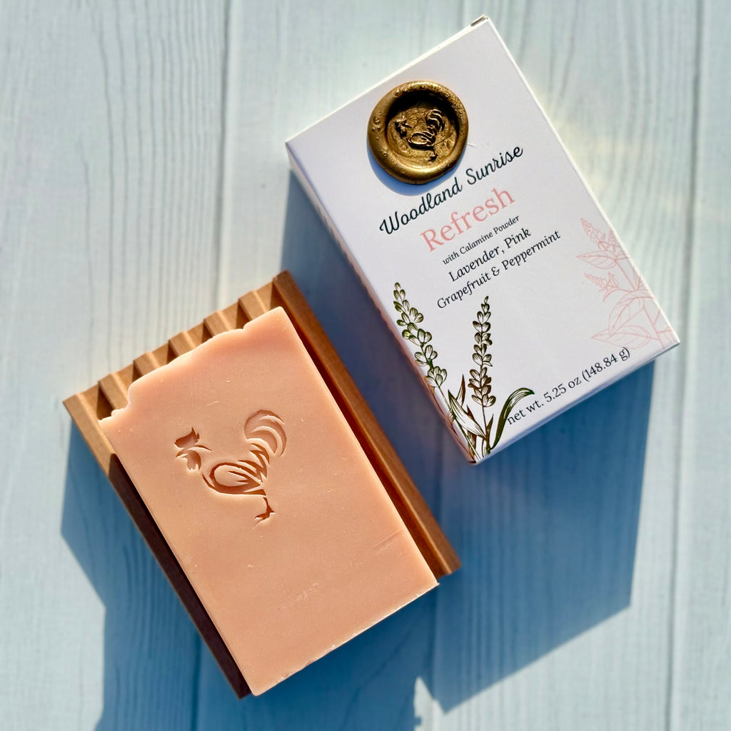 Bar of soap with a rooster design next to its packaging on a light blue wooden surface