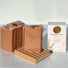 Three bars of soap on a wooden stand with a box labeled 'Woodland Sunrise' in the background.