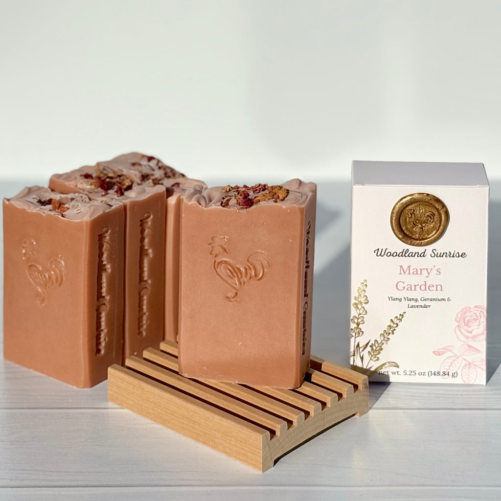 Three bars of soap on a wooden stand with a box labeled 'Woodland Sunrise' in the background.