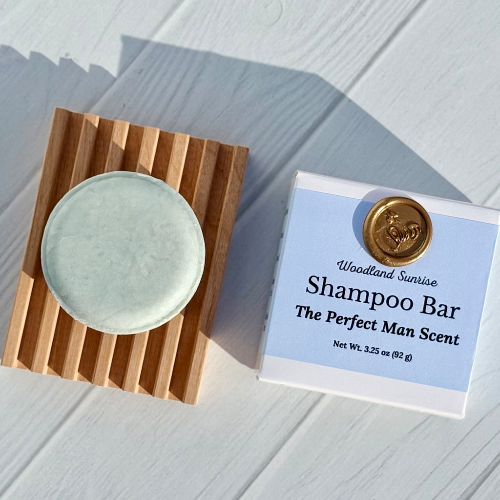 Shampoo bar on a wooden coaster with its packaging labeled 'Woodland Sunrise' on a light wooden surface.