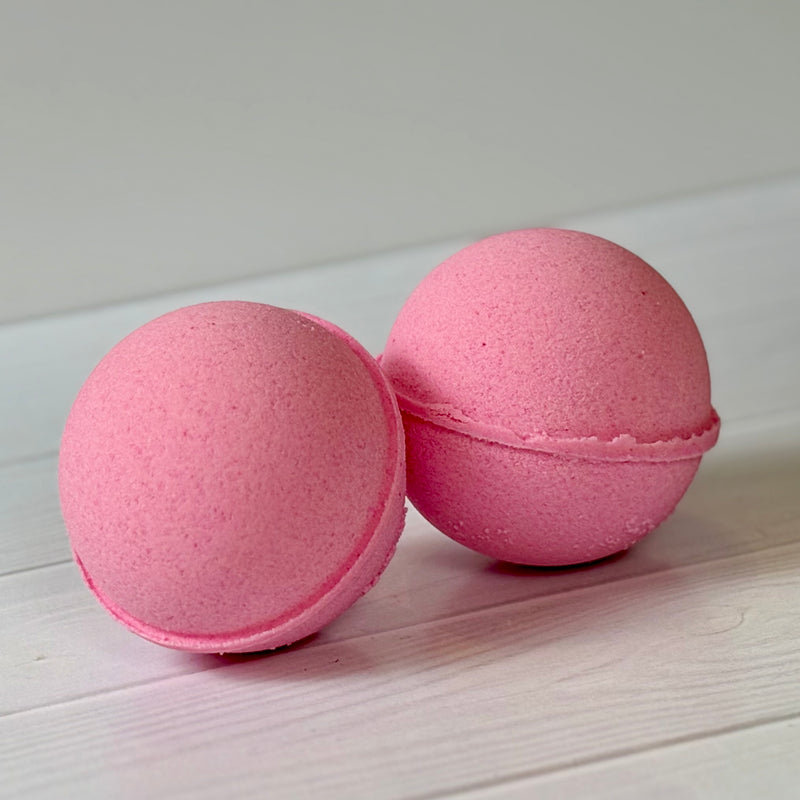Two pink bath bombs on a light wooden surface with a white background