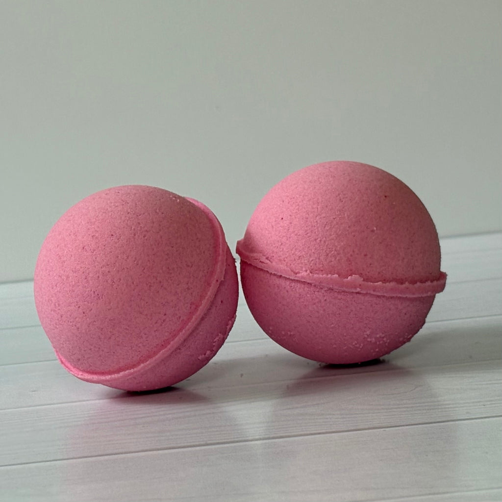 Two pink bath bombs on a light wooden surface with a white background