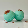 Two green bath bombs with decorative elements on a light wooden surface.