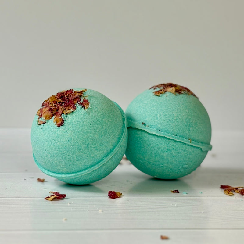 Two green bath bombs with decorative elements on a light wooden surface.