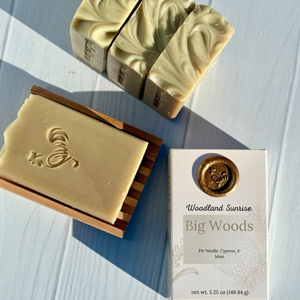 Two bars of soap and a box labeled 'Woodland Sunrise Big Woods' on a light wooden surface.