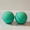 Two green bath bombs on a light wooden surface with a neutral background