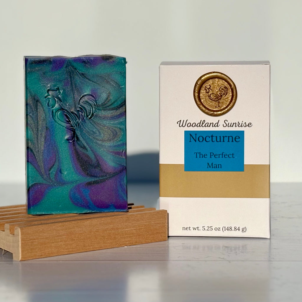 Bar of soap with a decorative design on a wooden stand next to its packaging labeled 'Woodland Sunrise Nocturne'.