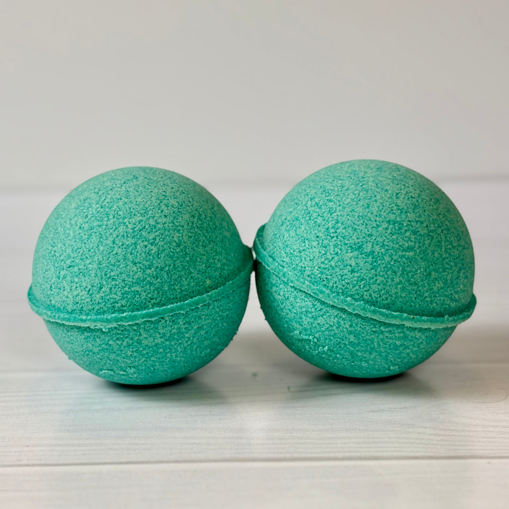 Two green bath bombs on a light wooden surface with a white background