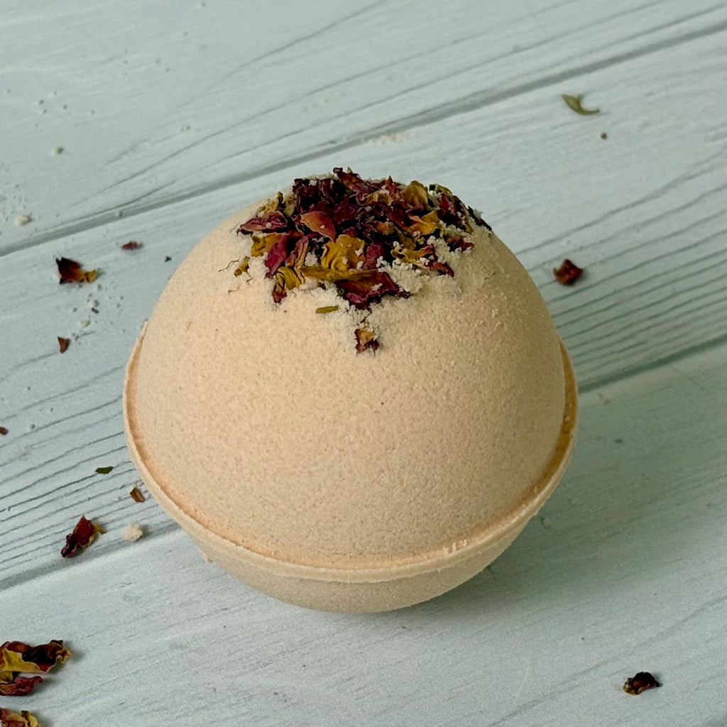 Pale pink bath bomb with dried herbs on a light wooden surface
